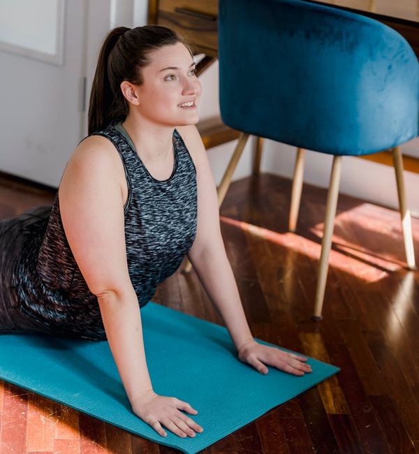 Smiling woman stretching gently on a yoga mat in a bright, sunlit room.
